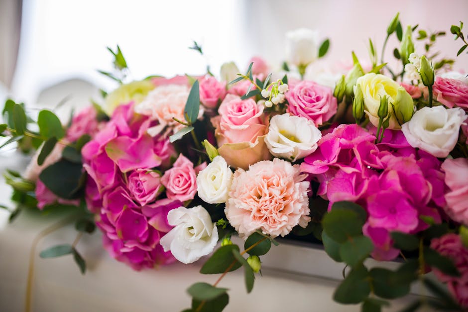 A vibrant floral arrangement featuring soft pink, white, and blush roses, complemented by pale peach carnations and creamy lisianthus, all nestled amidst lush green eucalyptus leaves. The bouquet is d